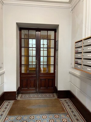 Una puerta doble de madera con paneles de vidrio, un tapete estampado y un archivador fijado a la pared.