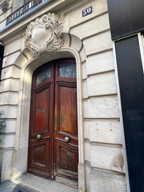Una doble puerta de madera con un arco decorativo encima, en un edificio de fachada de piedra.