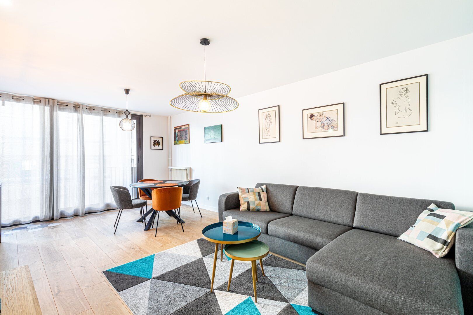 Un salon moderne avec un canapé gris, une table basse ronde et un coin repas comprenant une table et des chaises.