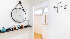 Un baño moderno con un espejo redondo, un estante negro con objetos decorativos y un mueble blanco.