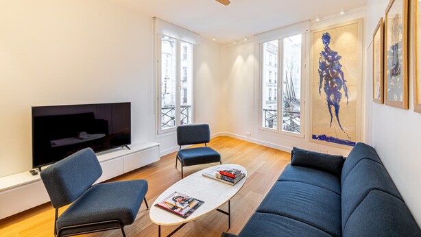 A modern living room with a flat-screen TV, two armchairs, a sofa, a coffee table, and a ceiling fan. - GuestReady - Modern apartment in a prime location (Paris)