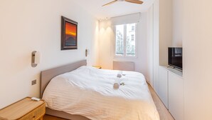 A modern bedroom with a bed, a ceiling fan, a TV, and a window with a view of buildings. - GuestReady - Modern apartment in a prime location (Paris)