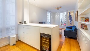 A modern kitchen with a central island, a built-in dishwasher, and a dining area with a blue sofa and a bookshelf. - GuestReady - Modern apartment in a prime location (Paris)