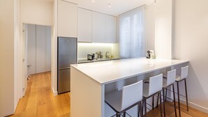 A modern kitchen with white cabinetry, a stainless steel refrigerator, a built-in oven, a sink, and a bar area with bar stools. - GuestReady - Modern apartment in a prime location (Paris)