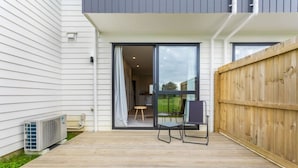 Eine Holzterrasse mit einer Schiebetür zu einem Zimmer, einem kleinen Tisch und einem Stuhl.