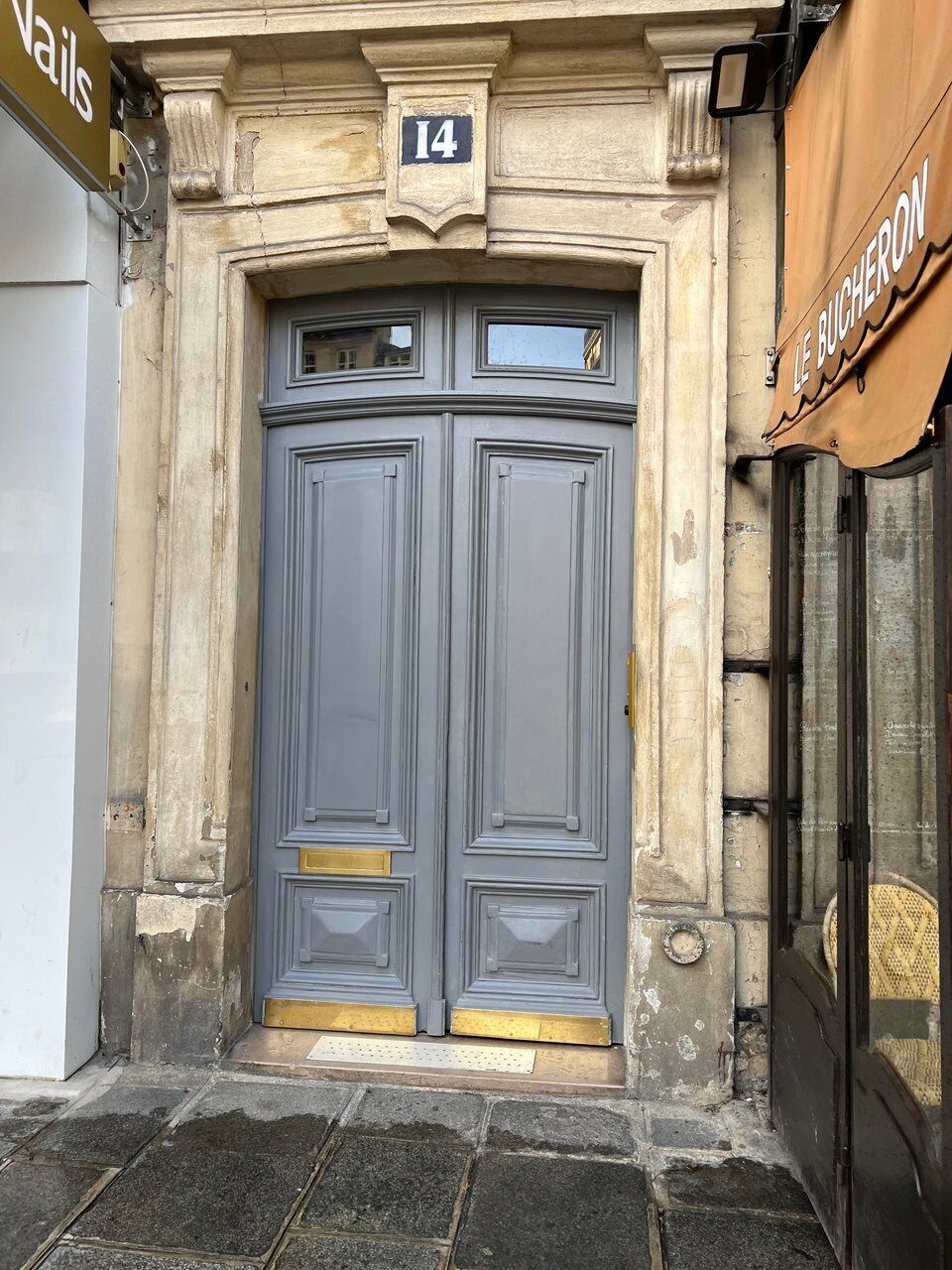 A double door with a number '14' above it, set in a stone facade with a metal gate to the right.