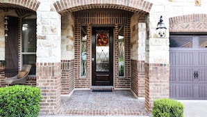 A brick house with a dark brown front door, a small porch, and a garage door. - The Views are for Miles! (San Antonio)