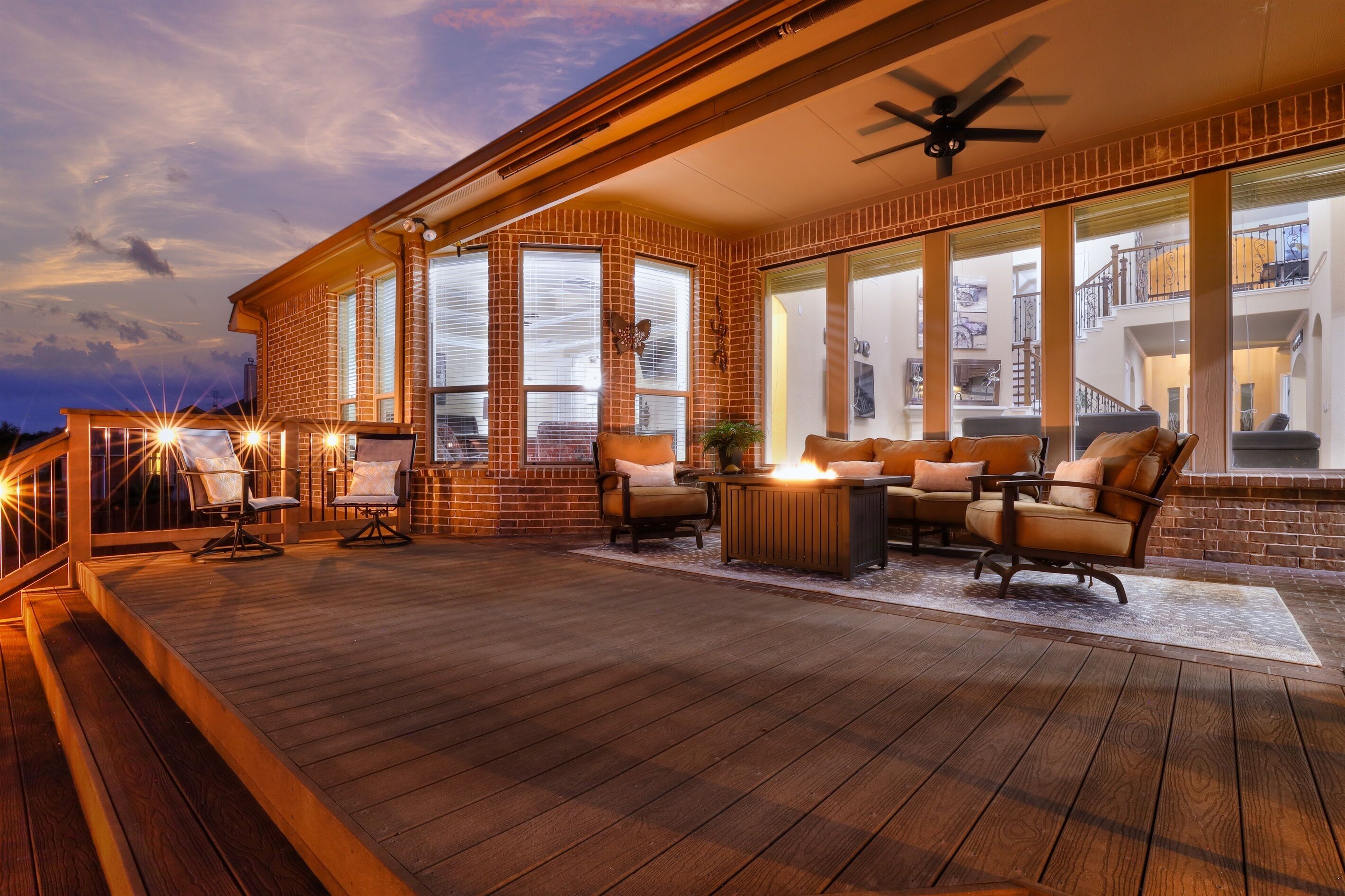A covered outdoor patio with wooden flooring, a ceiling fan, and a seating area with chairs and a table.