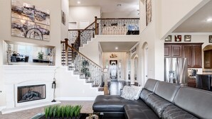 A spacious living area with a large black leather sofa, a fireplace, and a staircase leading to an upper level. - The Views are for Miles! (San Antonio)