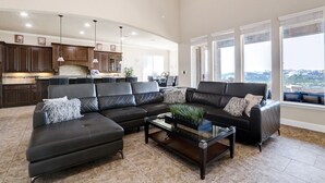 A spacious living room with a sectional sofa, a glass coffee table, and a view of the city through large windows. - The Views are for Miles! (San Antonio)