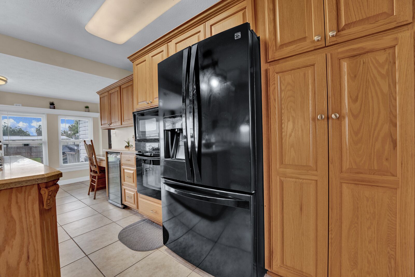 A kitchen with wooden cabinets, a black refrigerator, a built-in oven, and a dining area with a chair and table.