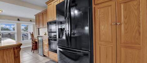 A kitchen with wooden cabinets, a black refrigerator, a built-in oven, and a dining area with a chair and table.