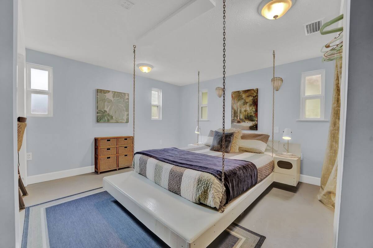 Un dormitorio con cama, mesitas de noche, una silla colgante y obras de arte en las paredes.