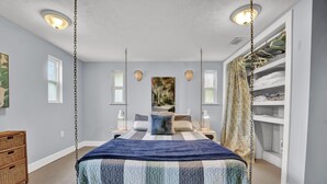 Un dormitorio con cama, mesitas de noche, una silla colgante y un armario.