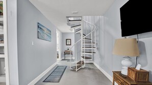 Un interior moderno con una escalera de caracol, una mesita de madera con una lámpara, y un cuadro enmarcado en la pared.