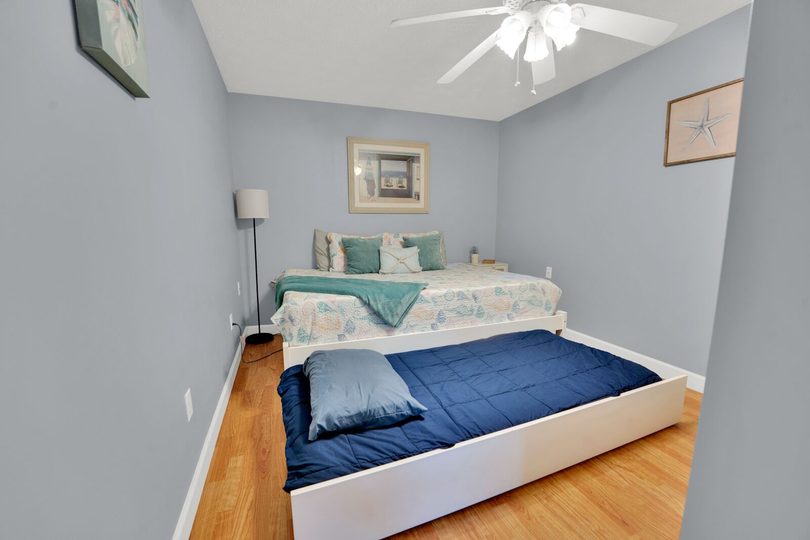 Une chambre à coucher avec un lit, un ventilateur de plafond et un tableau encadré accroché au mur.