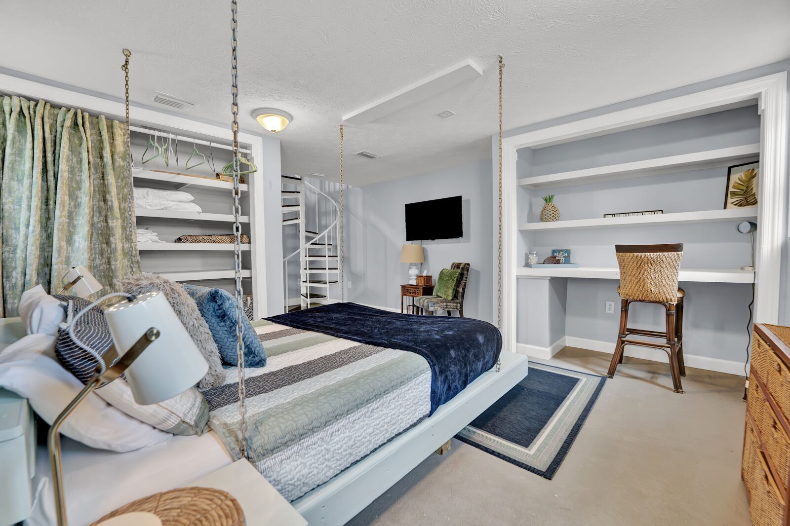 A bedroom with a bed, a chair, a desk, shelves, and a TV.
