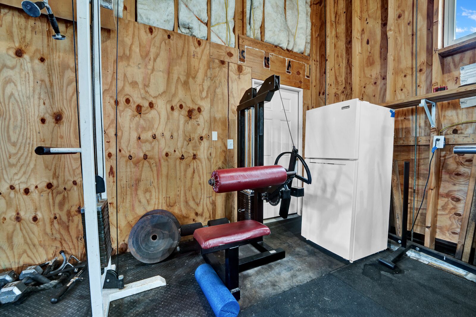 Et træningscenter med trævægge, bænkpres, squat stativ og et køleskab.