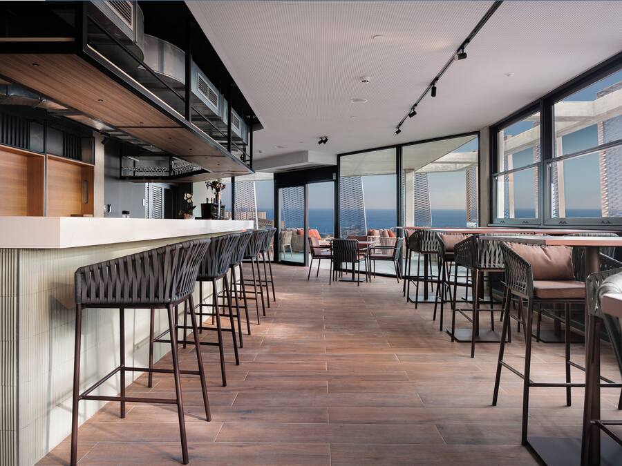 A modern bar area with high stools and a long counter, large windows offering a view of the cityscape.