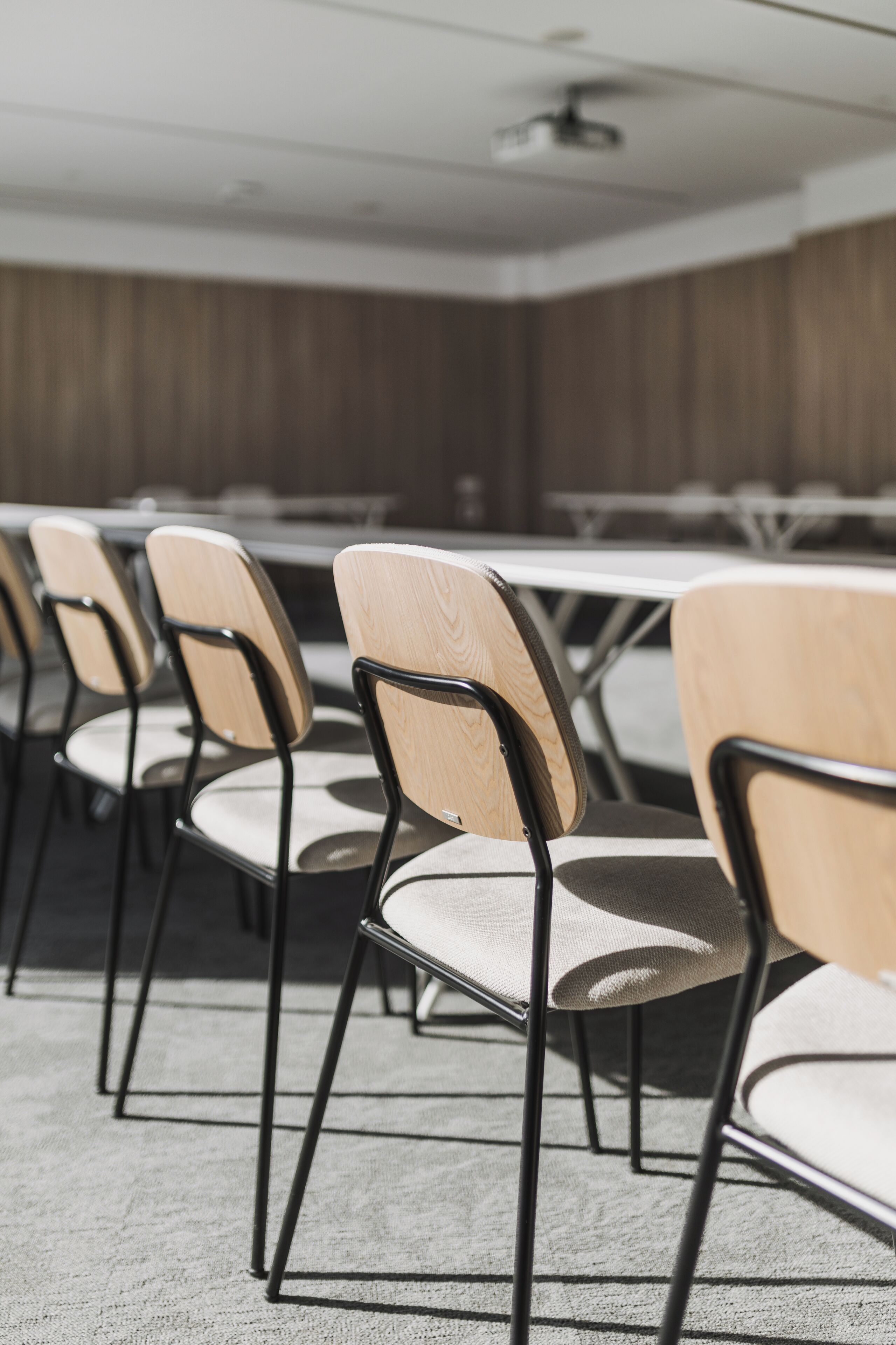 Un salón de conferencias con filas de sillas y mesas, paredes de paneles de madera y un ventilador de techo.