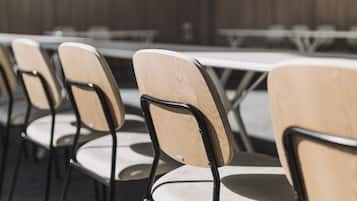 Un salón de conferencias con filas de sillas y mesas, paredes de paneles de madera y un ventilador de techo.