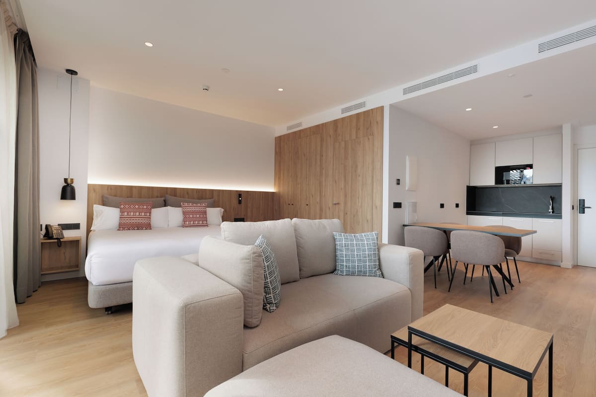 Una habitación de hotel moderna con sofá, una mesita, cama, escritorio y kitchenette.