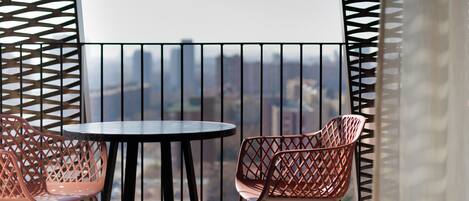 A balcony with a round table and two chairs, featuring a cityscape view through a patterned metal railing.