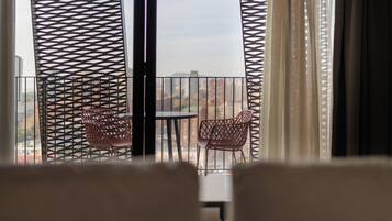 Un balcón con dos sillas y una mesa, visto a través de una ventana con celosía decorativa.
