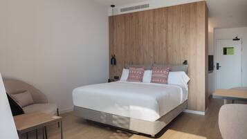 Una habitación de hotel moderna con un cabecero de madera, una cama con almohadas estampadas, una mesita pequeña y una silla.