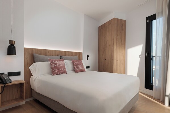 A modern bedroom with a large bed, a wooden wardrobe, a bedside table with a phone, and a window with curtains. - Hotel Tembo Barcelona (Sant Adria de Besos)