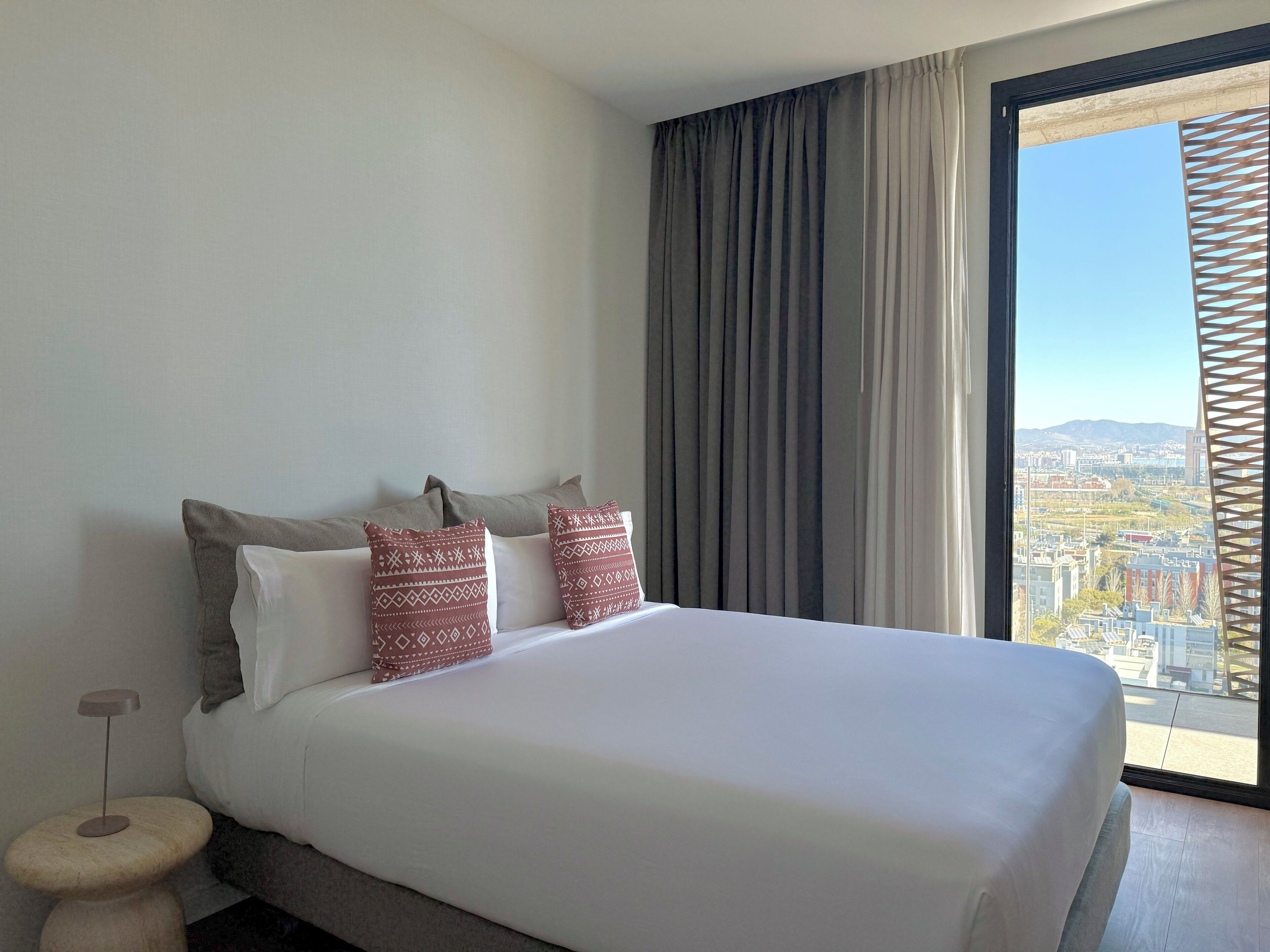 A hotel room with a large bed, a view of the city through a window, and a decorative wooden panel.