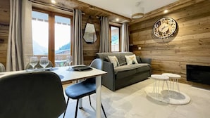 A cozy living room with a sofa, a dining table with chairs, a fireplace, and a large wall clock. - N°12 : 4 people flat with balcony, incl. swimmingpool, sauna, hammam (CHAMPAGNY EN VANOISE)