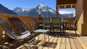 A wooden deck with chairs and a table, overlooking snow-capped mountains.