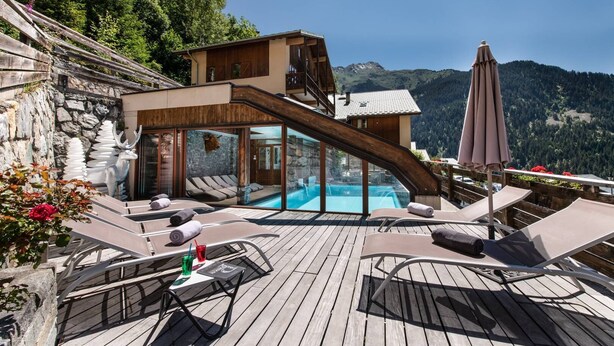 A wooden deck with lounge chairs and a pool area, overlooking a mountainous landscape.
