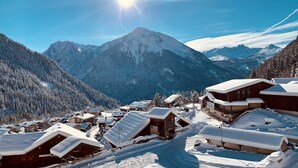 Un pueblo cubierto de nieve con edificios de madera, cielo despejado y un pico montañoso destacado al fondo.