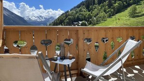 Una terraza de madera con recortados en forma de corazón, una mesa con sillas y vistas a una cordillera.