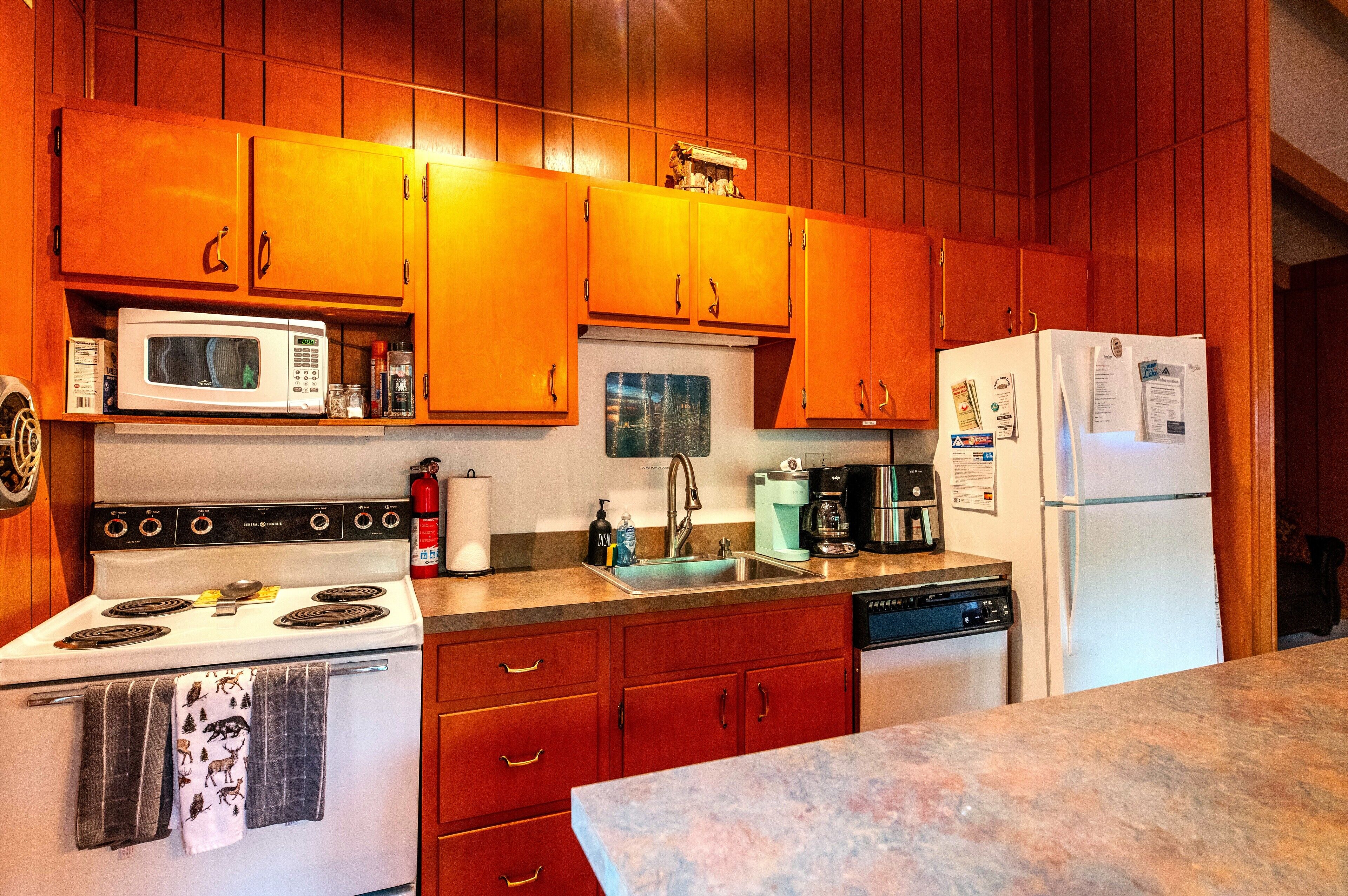A kitchen with wooden cabinets, a white stove, a microwave, a sink, and a refrigerator.