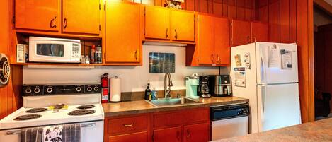 A kitchen with wooden cabinets, a white stove, a microwave, a sink, and a refrigerator.