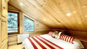 Une chambre avec un plafond en pente, des murs en bois, une grande fenêtre et un lit avec une literie à rayures.