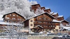 A multi-story lodge with a ski slope in the background. - N°30 : 4 people mezzanine studio incl. swimmingpool, sauna, hammam (CHAMPAGNY EN VANOISE)