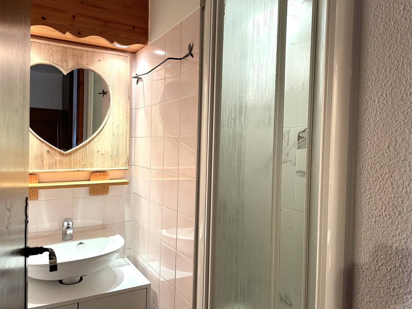 Une salle de bain avec un lavabo blanc, un miroir rond et une cabine de douche en verre.