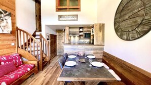 A wooden interior with a dining table set for four, a staircase, and a kitchen area.