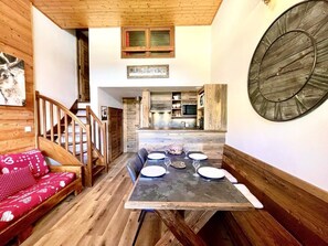 A wooden interior with a dining table set for four, a staircase, and a kitchen area.