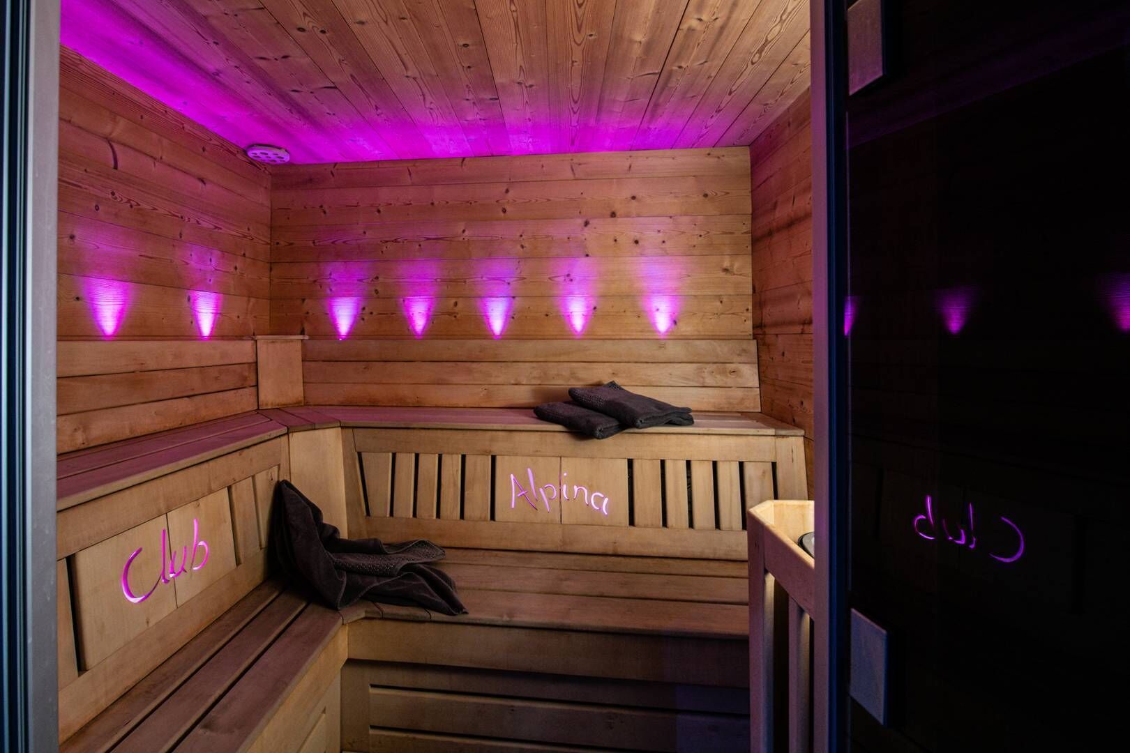 A wooden sauna with benches and benches, purple lighting, and a neon sign reading "Aprica".