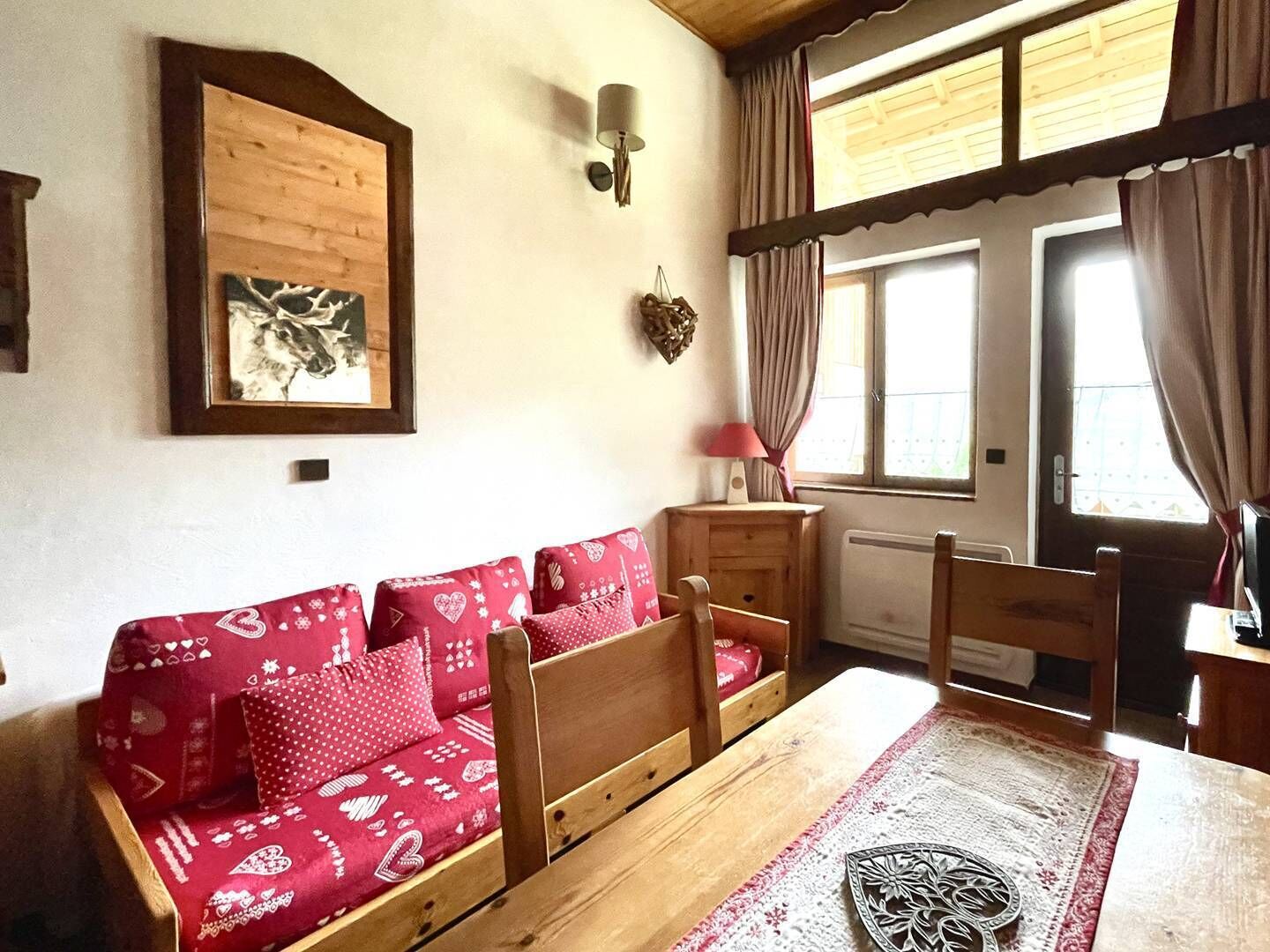 A cozy room with a wooden sofa, a table, and a window with curtains.