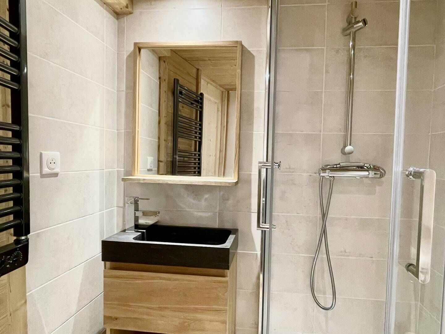 Ein modernes Badezimmer mit einem Holzbadezimmermöbel, einer Duschkabine aus Glas und einem Spiegel über dem Waschbecken.