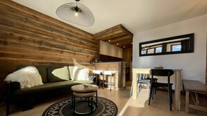 A modern living room with a wooden accent wall, a round coffee table, a sofa with fluffy cushions, and a dining area with a table and chairs. - N°34 : 6/7 people flat incl. swimmingpool, sauna, hammam (CHAMPAGNY EN VANOISE)