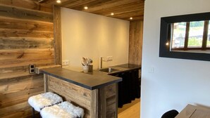 A kitchen with a wooden accent wall, a bar area with stools, and a window with a view. - N°34 : 6/7 people flat incl. swimmingpool, sauna, hammam (CHAMPAGNY EN VANOISE)