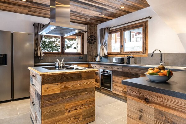 A modern kitchen with a wooden island, stainless steel appliances, and a large window providing natural light. - St Maurice : 5* chalet with private pool et jacuzzi (CHAMPAGNY EN VANOISE)
