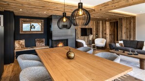 A modern living room with a wooden dining table, two sofas, a fireplace, and a TV mounted on the wall.
